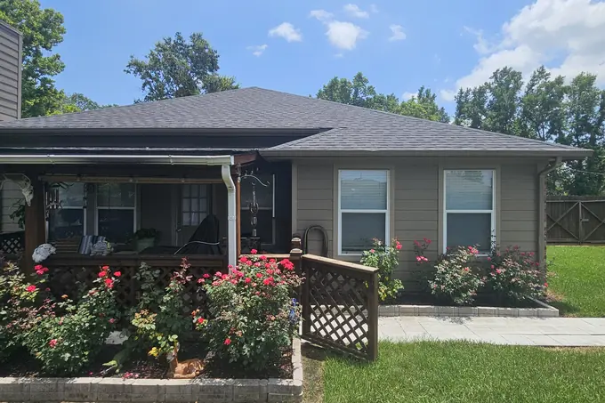 Shingle roof above a house with a porch and flowering shrubs